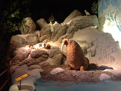 [A taxidermied walrus sits at the water's edge while the 'eskimos' are further back behind some rocks.]